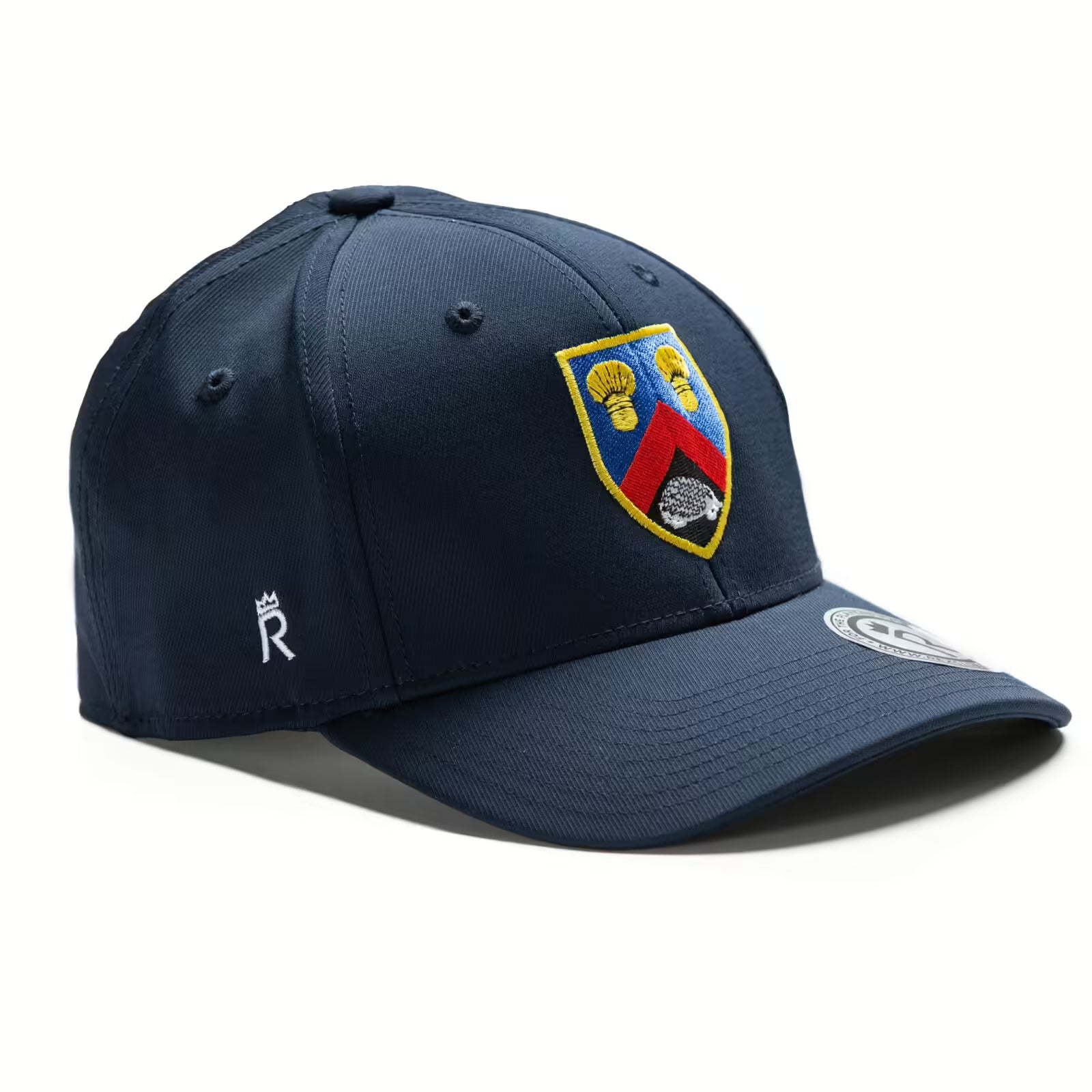 Rex Club | The Rex Club Alderley Edge CC Stretch is a navy baseball cap with an embroidered shield crest—two yellow flowers and a red chevron—Cheshire-inspired, a small white "R" on the side, and a round tag on the brim. | Custom Caps | Custom Hats | Team Headwear | UK