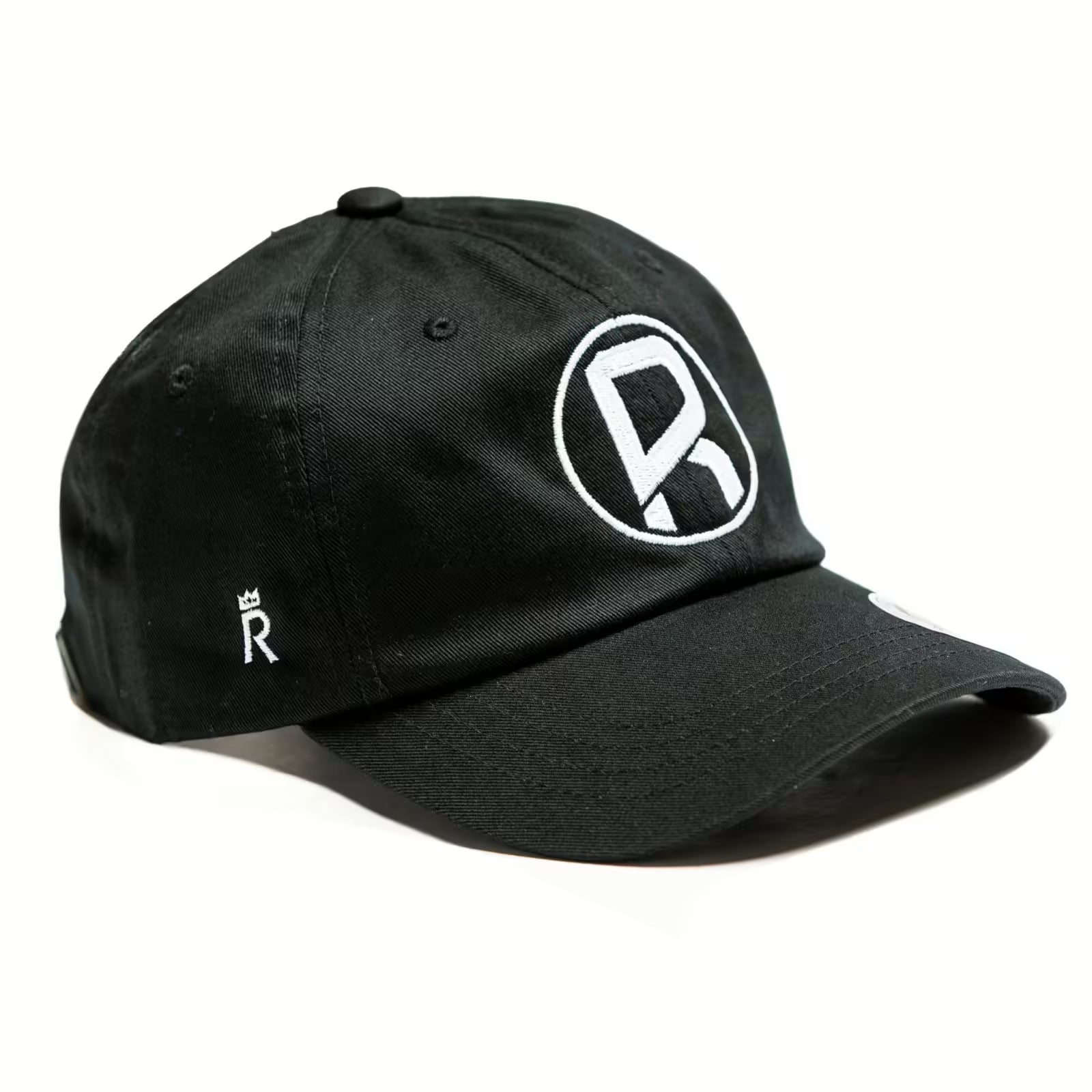 Rex Club | The Rugby Pod Trucker Slouch by Rex Club is a black cap with a bold white "R" logo in a circle on the front and a small crowned "R" emblem on the side, perfect for rugby fans, shown against a white background. | Custom Caps | Custom Hats | Team Headwear | UK