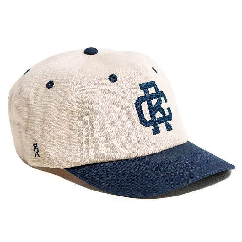 Rex Club | The Rex Club - TwoTone - Canvas Cap is a beige 100% cotton cap with a navy brim, navy top button and eyelets, "DC" embroidery on the front, a small "R" logo on the side, and an adjustable fit for most sizes. | Custom Caps | Custom Hats | Team Headwear | UK