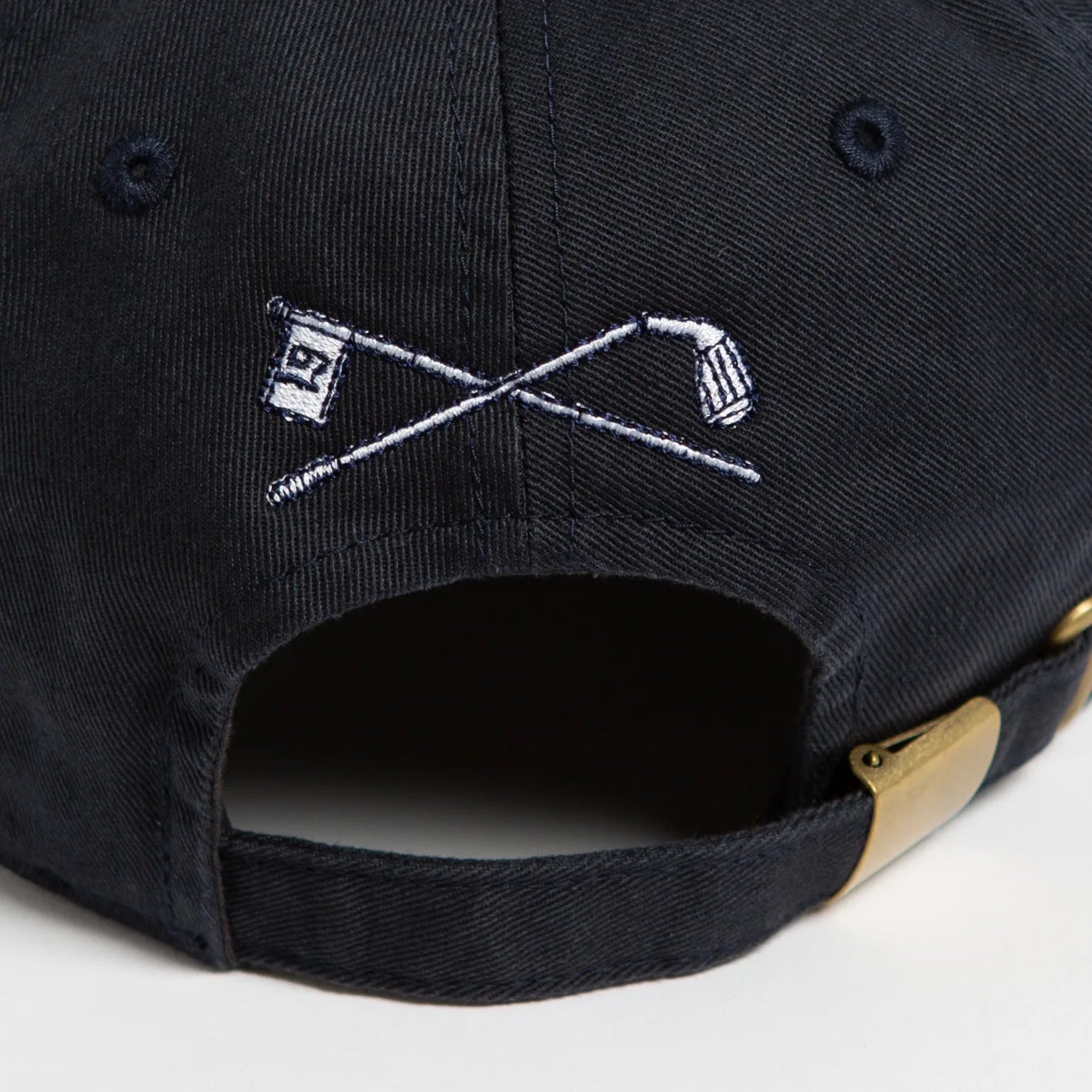 Rex Club | Close-up of the back of the Rex Club Golf: Quiet Please - Navy, Slouch cap, showcasing an embroidered crossed golf club and a flag with the number 19 design. The cap includes a brass adjustment buckle for a perfect fit. | Custom Caps | Custom Hats | Team Headwear | UK