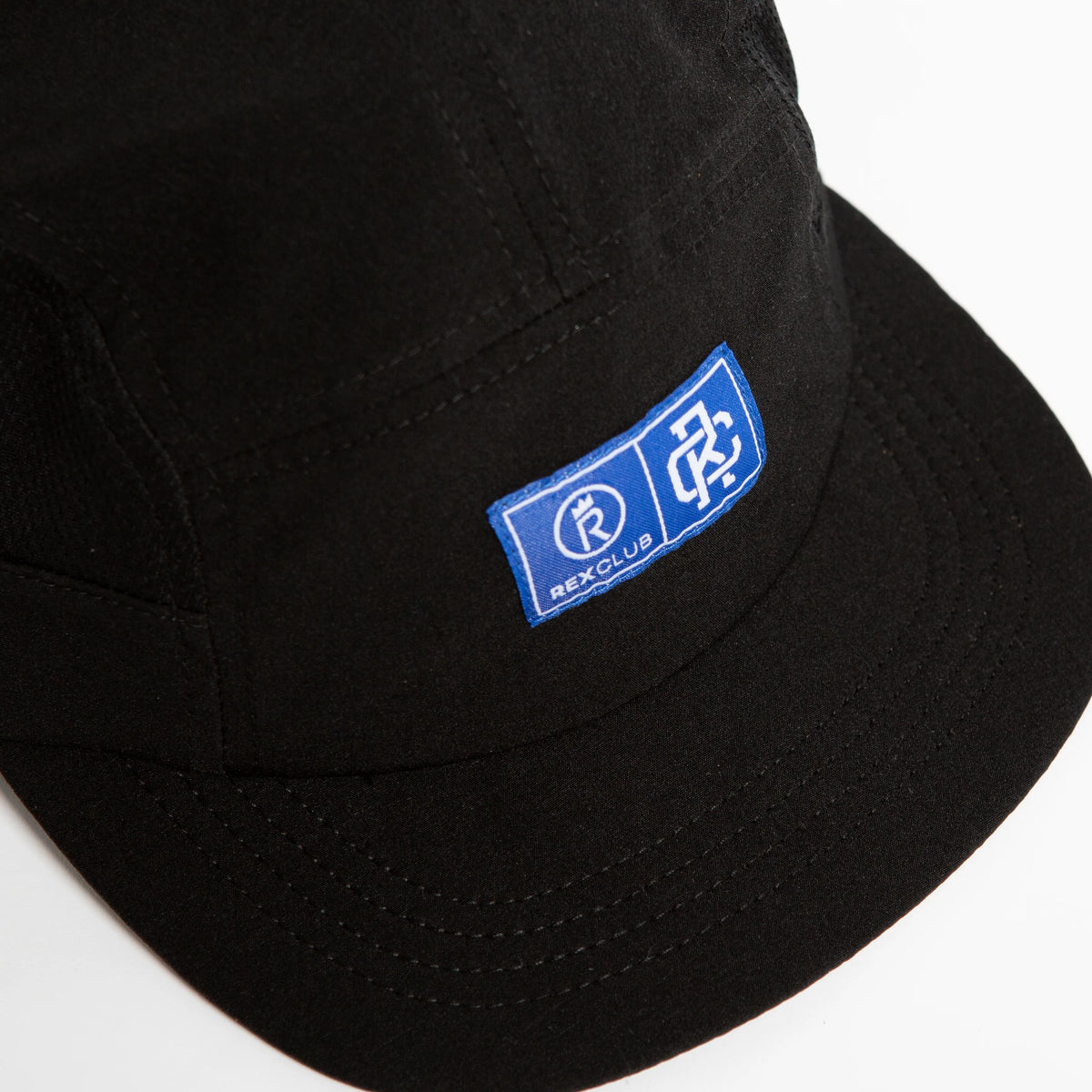 Rex Club | A black polyester Running Cap by Rex Club featuring a blue rectangular patch with white graphic symbols and "REXCLUB" text on the front. The close-up image highlights the patch and the cap’s bill. | Custom Caps | Custom Hats | Team Headwear | UK