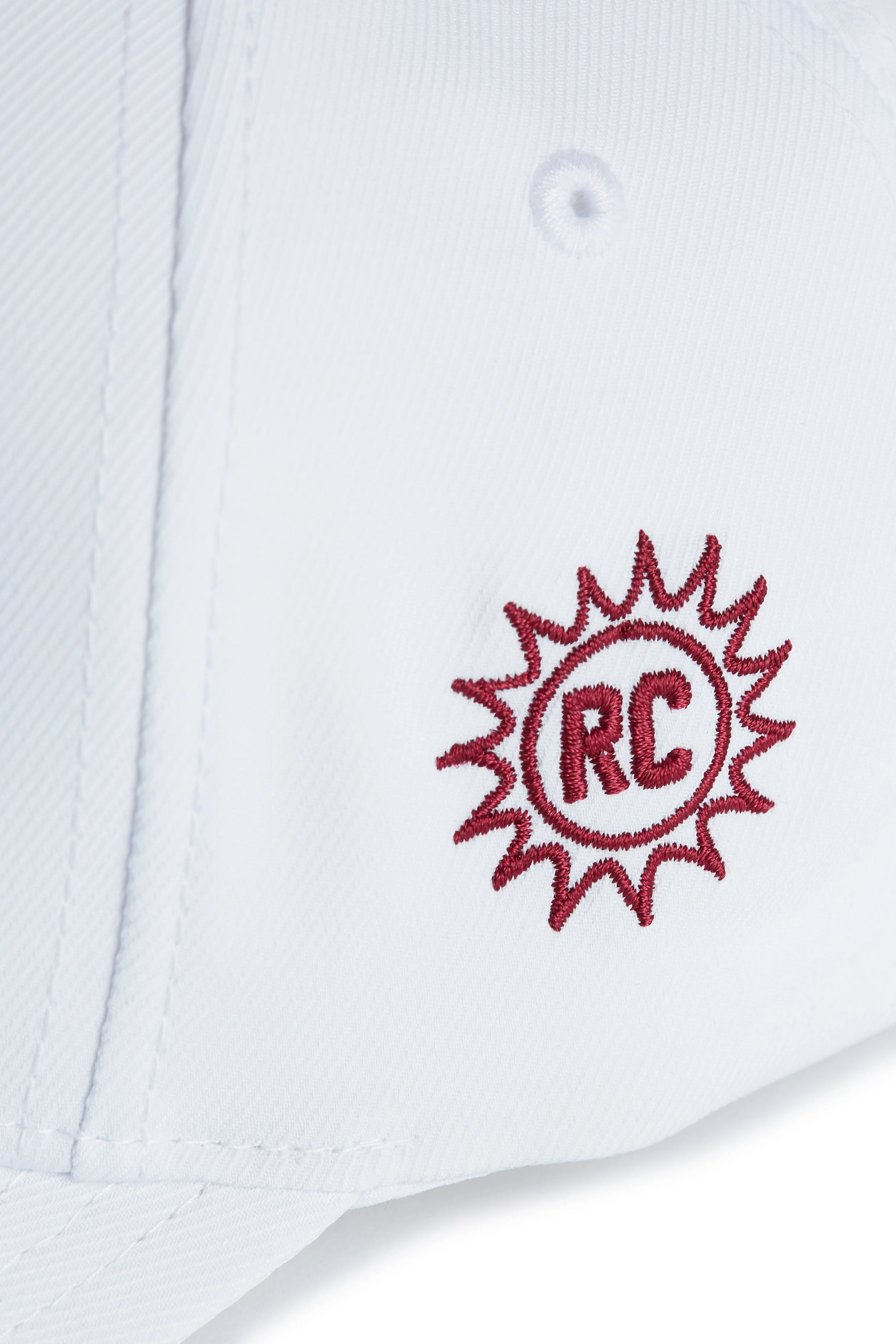 Rex Club | Close-up of a navy performance cap from Rex Club, featuring a red embroidered sunburst design with the letters "RC" in the center—part of the exclusive OFFSEASON 26 collection. | Custom Caps | Custom Hats | Team Headwear | UK