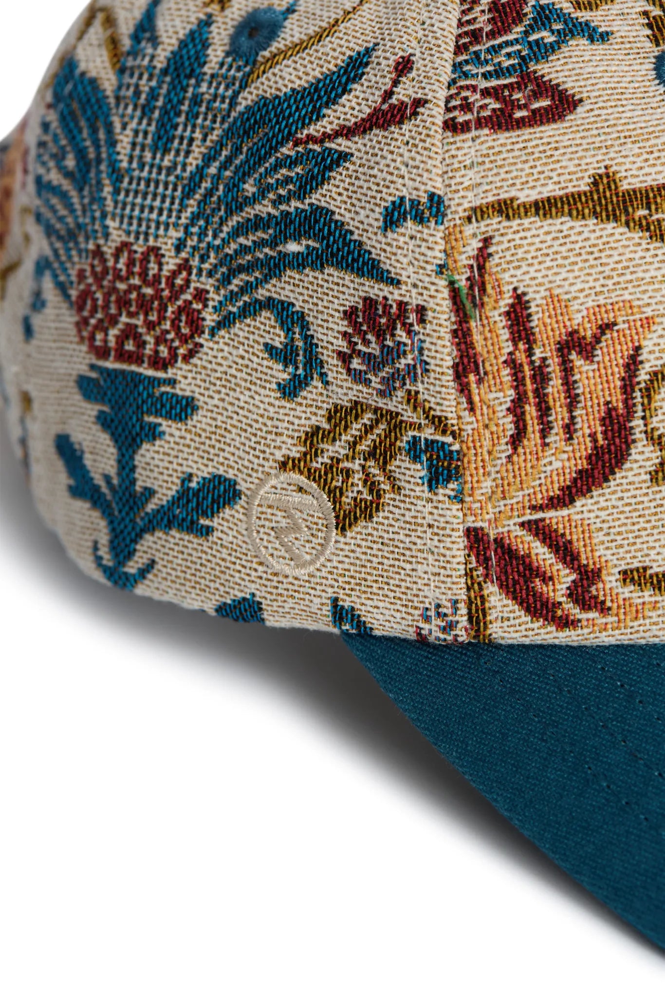 Rex Club | Close-up of the Rex Club "A New Day" cap, featuring a blue, red, and gold floral tapestry on beige with a solid teal bill. The woven fabric’s texture showcases the premium quality of this bespoke accessory. | Custom Caps | Custom Hats | Team Headwear | UK variant-1