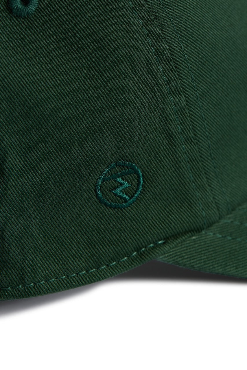 Rex Club | Close-up of the MTRC - Green club cap by Rex Club, crafted from dark green cotton and featuring a small embroidered circle logo with a lightning bolt near the brim—a refined detail that distinguishes this cap. | Custom Caps | Custom Hats | Team Headwear | UK