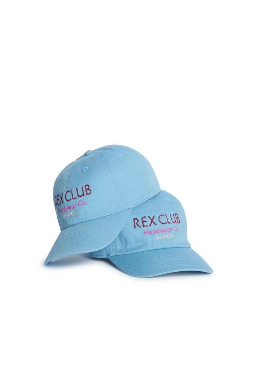 Rex Club | Two “In the details - Cornflower” slouch caps by Rex Club, featuring light blue fabric and “REX CLUB Headwear Co. MMXIII” embroidered in purple and pink, stacked on a white background. | Custom Caps | Custom Hats | Team Headwear | UK