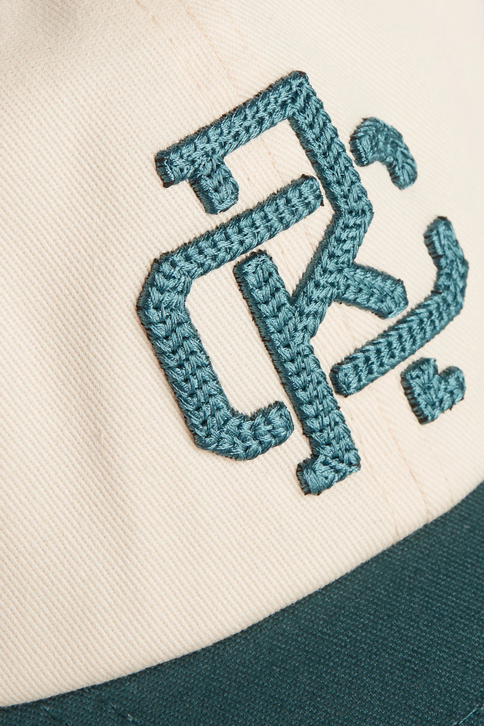 Rex Club | Close-up of the RC - Two/Tone - SS26 Green cap by Rex Club, a beige 100% cotton one-size-fits-most cap featuring dark green stitched embroidery with stylized letters and a matching dark green brim. | Custom Caps | Custom Hats | Team Headwear | UK