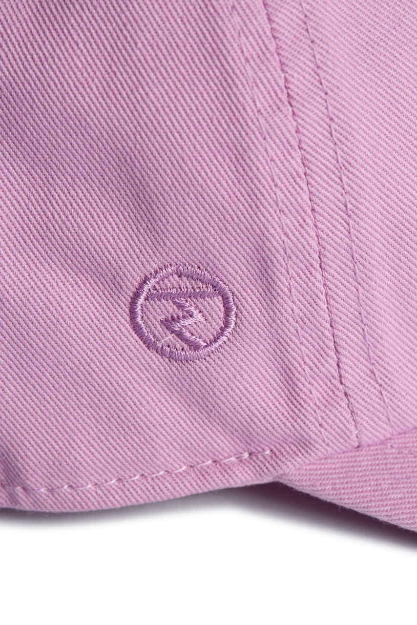 Rex Club | Close-up of the Rex Club “In the details - Parma Violet” cap, showcasing pink fabric with visible stitching and an embroidered circular logo featuring a stylized “R” in the center. | Custom Caps | Custom Hats | Team Headwear | UK