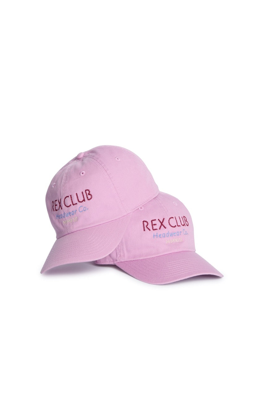 Rex Club | Two “In the details - Parma Violet” slouch caps by Rex Club, crafted from 100% cotton in pastel pink with “REX CLUB Headwear Co.” embroidered in red and blue on the front, are displayed on a white background—one cap resting atop the other—making them the perfect summer hats for any occasion. | Custom Caps | Custom Hats | Team Headwear | UK