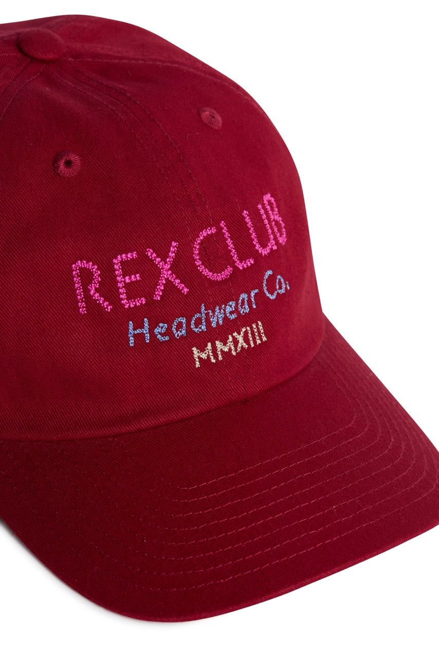 Rex Club | Add a vibrant touch to your summer hats collection with the “In the details - Tyrian” cap by Rex Club—a red baseball cap crafted from 100% cotton, featuring “REX CLUB Headwear Co. MMXIII” embroidered on the front in pink, blue, and yellow thread. | Custom Caps | Custom Hats | Team Headwear | UK
