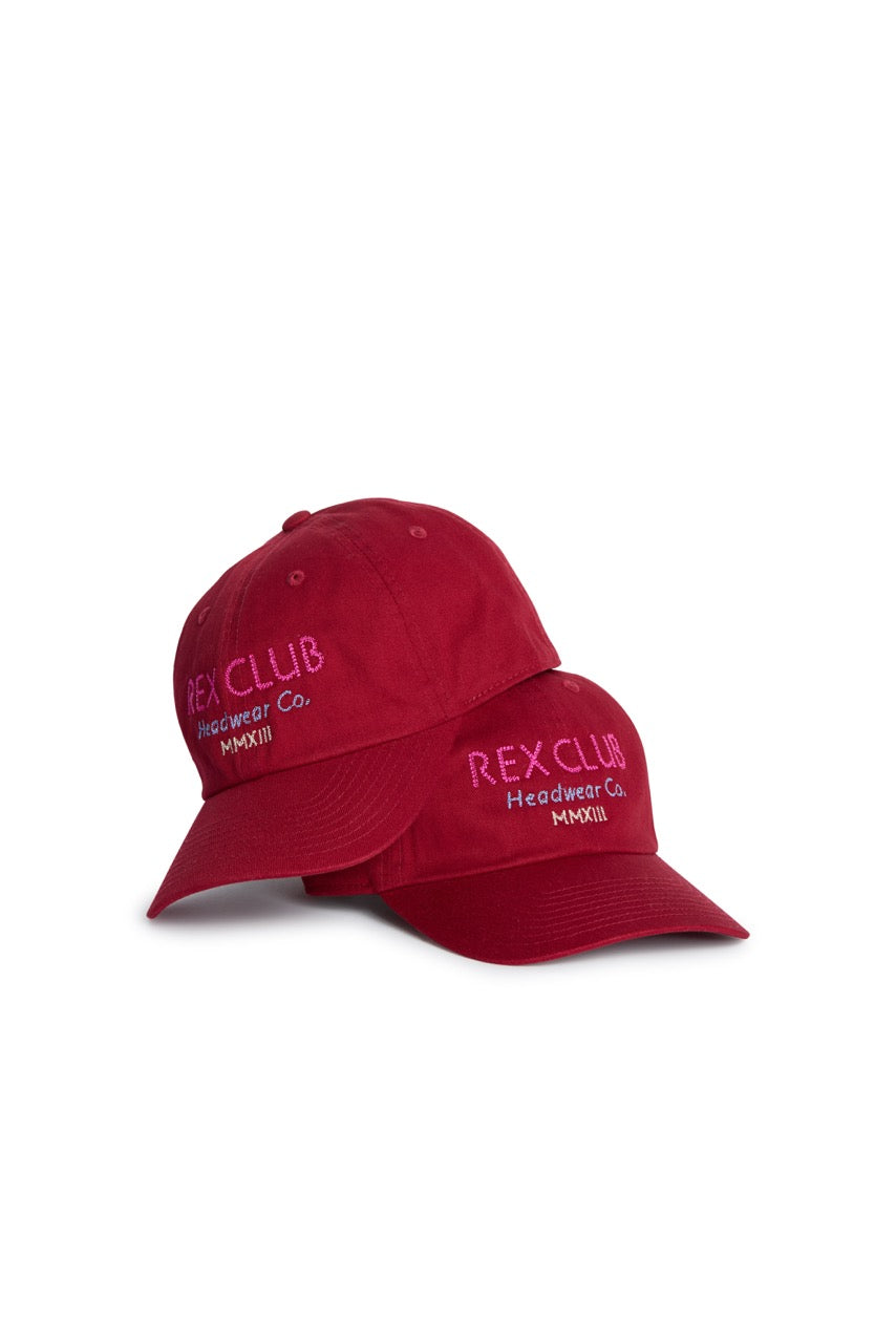 Rex Club | Two red “In the details - Tyrian” baseball caps from Rex Club are stacked together, each displaying pink embroidered “REX CLUB Headwear Co. MMXIII” text on the front panels against a white background. Crafted from 100% cotton, these summer hats effortlessly combine comfort and style for any casual outing. | Custom Caps | Custom Hats | Team Headwear | UK