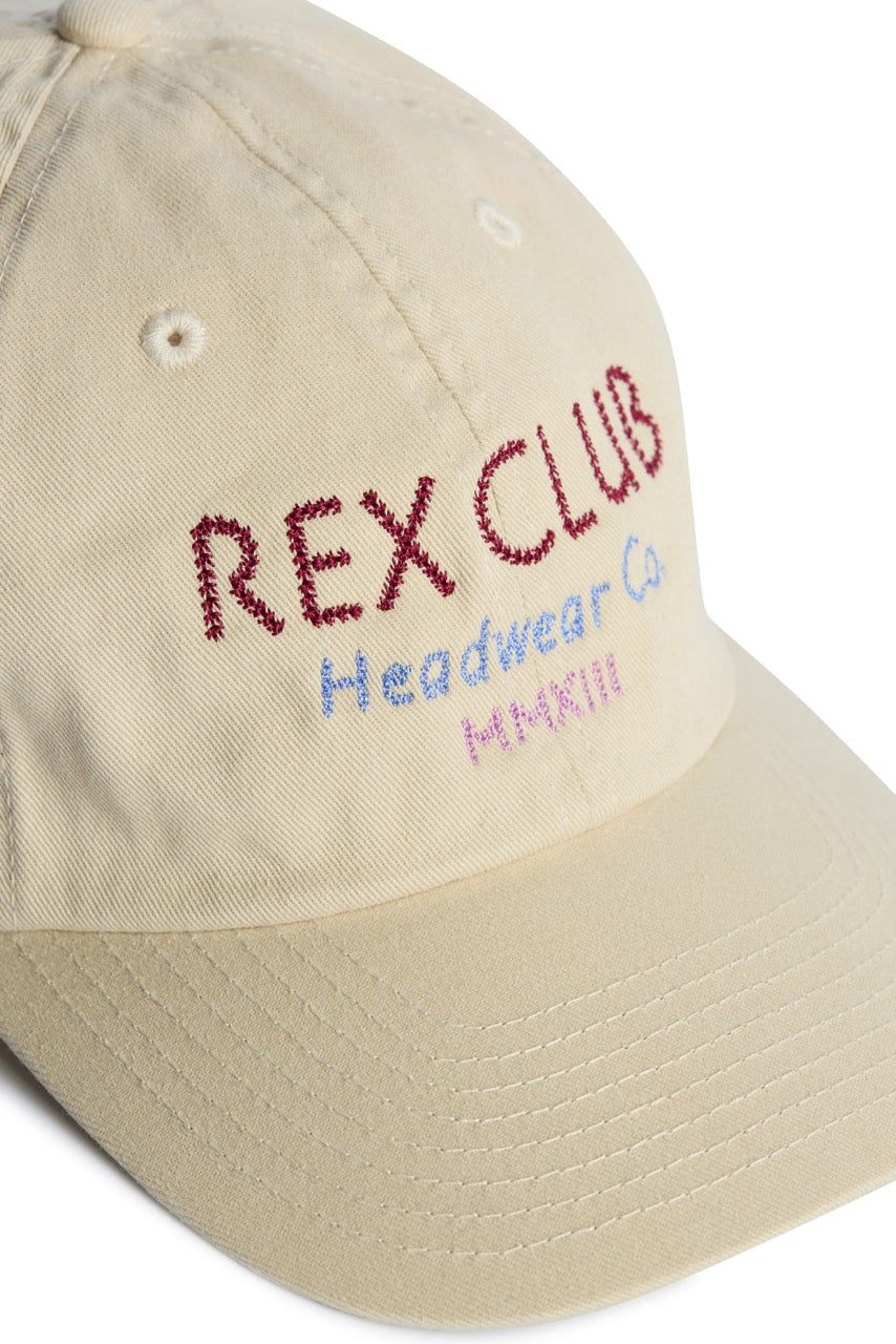 Rex Club | Introducing the “In the details - Cotton” cap by Rex Club—a 100% cotton beige baseball cap highlighted by red, blue, and pink embroidered “REX CLUB Headwear Co. Hatfill” text on the front panel. This stylish slouch cap makes a perfect summer accessory for those seeking fashionable headwear. | Custom Caps | Custom Hats | Team Headwear | UK