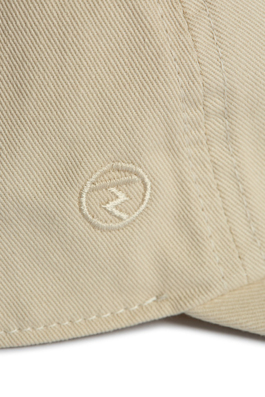 Rex Club | Close-up of beige 100% cotton fabric from Rex Club’s “In the details - Cotton” collection, featuring visible stitching and a small embroidered logo—a circle with a zigzag line inside—commonly seen on their stylish slouch caps and summer hats. | Custom Caps | Custom Hats | Team Headwear | UK
