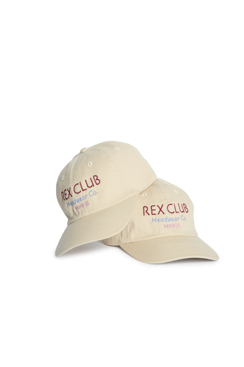 Rex Club | Two beige slouch caps from Rex Club, part of the ‘In the details - Cotton’ collection, featuring “REX CLUB Headwear Co. MMXIII” embroidered in purple and orange on the front, stacked on a white background. Made from 100% cotton, these summer hats provide comfort and style for any occasion. | Custom Caps | Custom Hats | Team Headwear | UK
