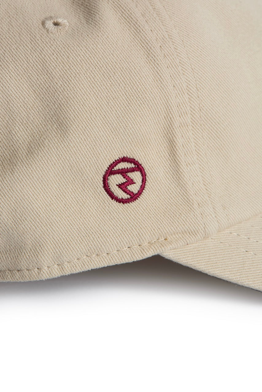 Rex Club | A close-up of the Rex Club RC 3d 26 - Beige cotton slouch cap, showcasing a small, circular red 3D embroidered logo with a stylized lightning bolt inside. | Custom Caps | Custom Hats | Team Headwear | UK