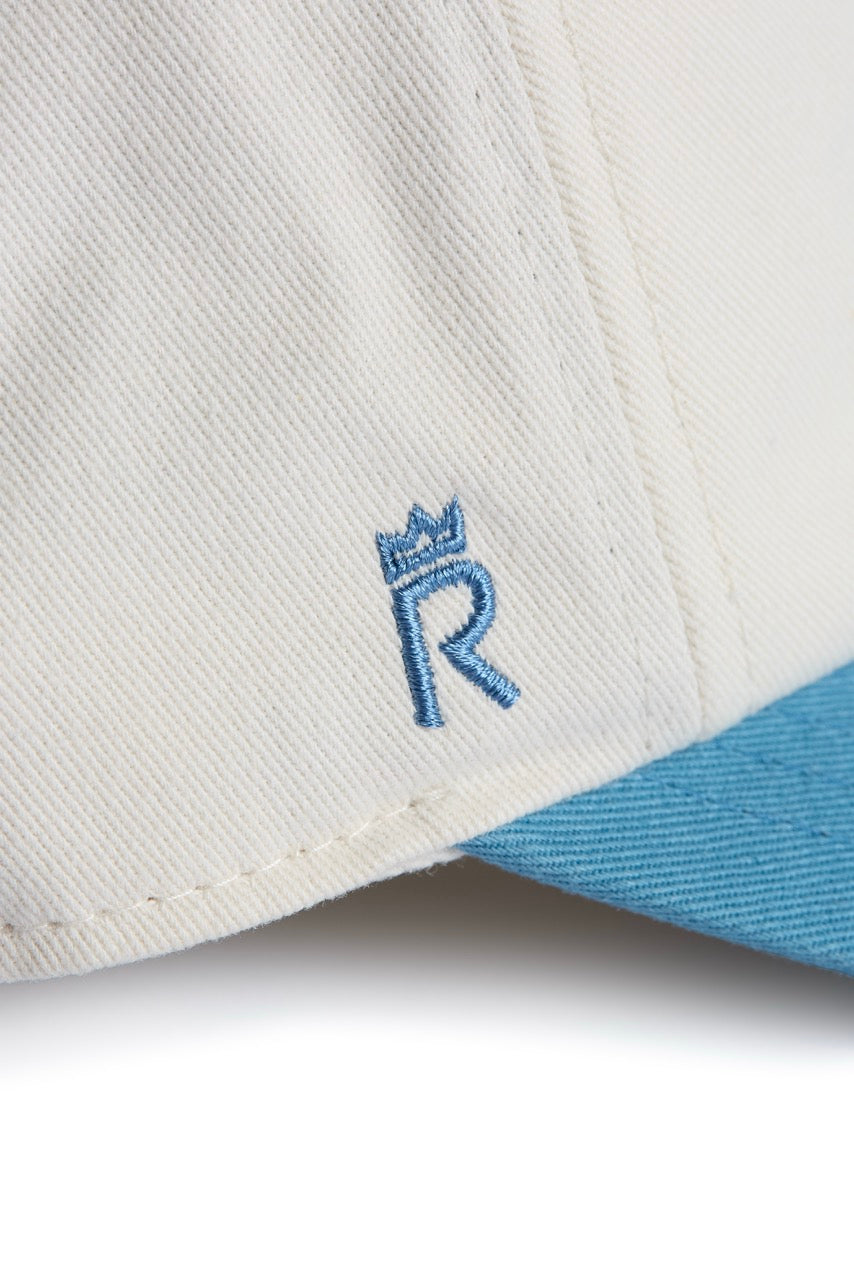 Rex Club | A close-up of the Rex Club Exeter Chiefs - Two Tone cap showcases its white crown with a light blue brim, featuring a blue embroidered letter “R” topped with a small crown on the front panel. Crafted from 100% cotton for comfort and durability, this is a true premium bespoke product. | Custom Caps | Custom Hats | Team Headwear | UK
