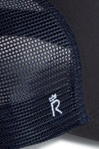 Rex Club | Close-up of the RC 26 Trucker by Rex Club, a navy blue mesh hat with a small white embroidered "R" monogram and crown symbol on the mesh side panel, inspired by the iconic Rex Club style. | Custom Caps | Custom Hats | Team Headwear | UK