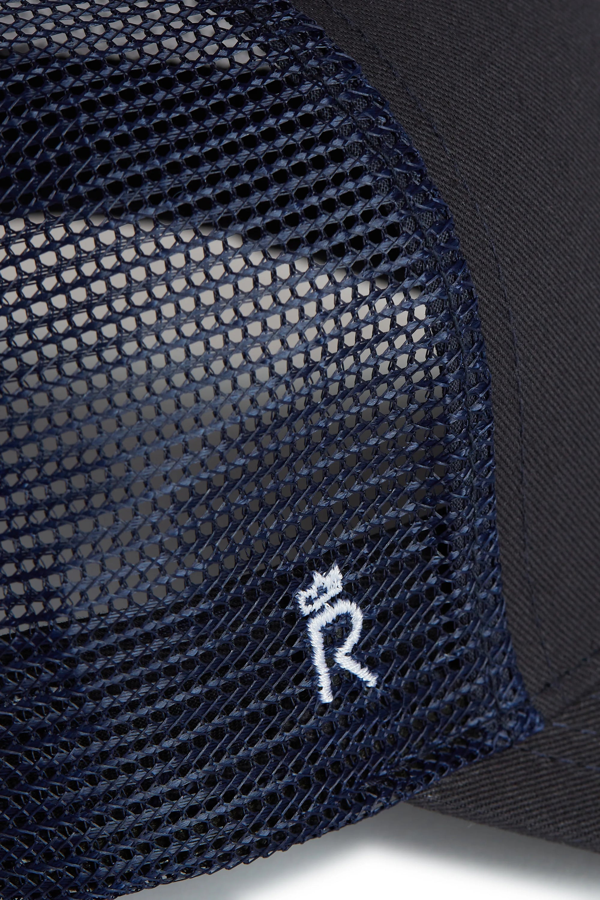 Rex Club | Close-up of the RC 26 Trucker by Rex Club, a navy blue mesh hat with a small white embroidered "R" monogram and crown symbol on the mesh side panel, inspired by the iconic Rex Club style. | Custom Caps | Custom Hats | Team Headwear | UK