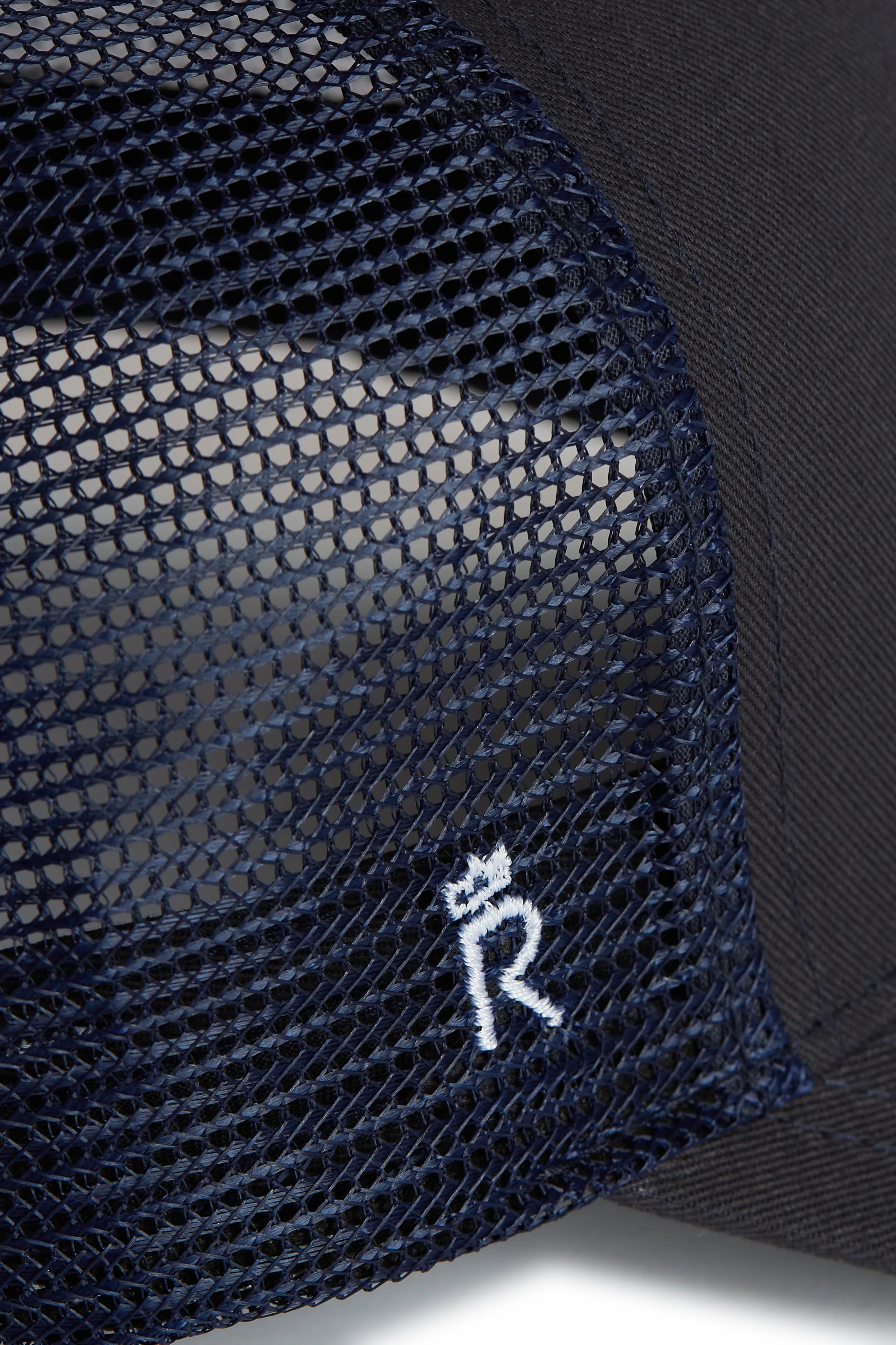 Rex Club | Close-up of the RC 26 Trucker by Rex Club, a navy blue mesh hat with a small white embroidered "R" monogram and crown symbol on the mesh side panel, inspired by the iconic Rex Club style. | Custom Caps | Custom Hats | Team Headwear | UK