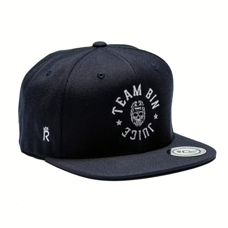 Rex Club | The Rex Club "Team Bin Juice Benchwarming" Snapback in navy features white embroidered "TEAM BIN JUICE" text and a skull with glasses and hat on the front, plus a small white logo on the side and a sticker on the flat brim. | Custom Caps | Custom Hats | Team Headwear | UK