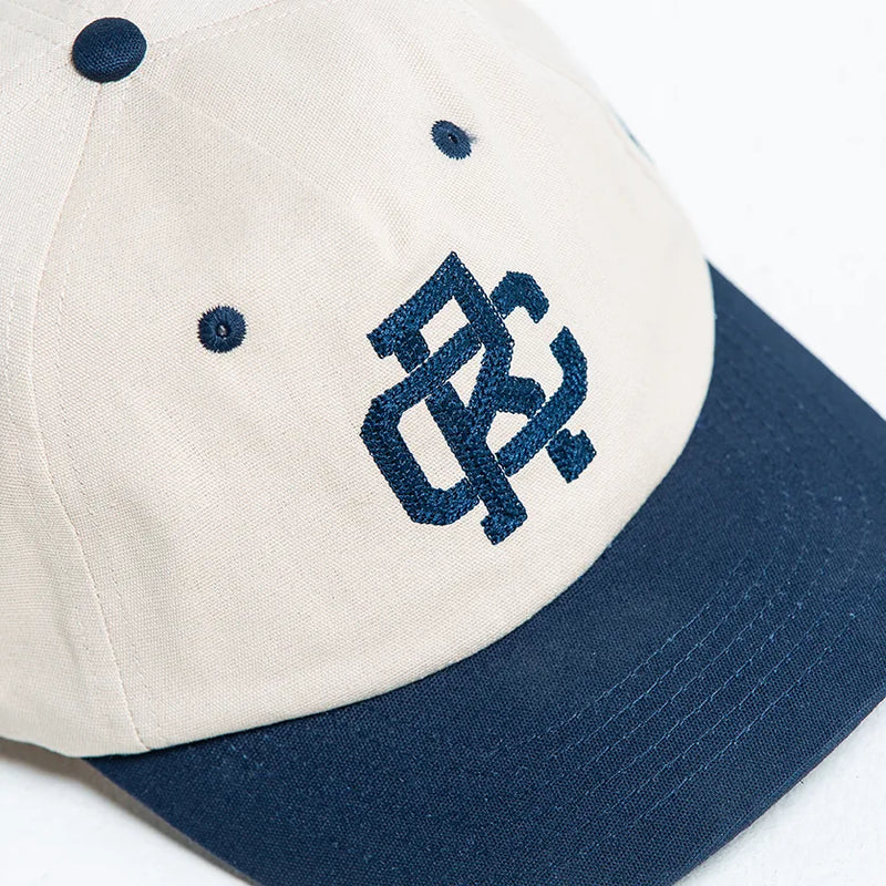 Rex Club | The Rex Club - TwoTone - Canvas Cap is a 100% cotton baseball cap with beige panels, a navy brim and button, and a dark blue embroidered "BC" logo on the front. One size fits most. Brand: Rex Club. | Custom Caps | Custom Hats | Team Headwear | UK