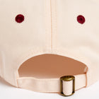 Rex Club | Close-up of the back of the RC - Victor - Two Tone baseball cap by Rex Club, showing red embroidered eyelets and an adjustable strap with a brass-colored clasp engraved "REX." Light beige cotton. One size fits most. | Custom Caps | Custom Hats | Team Headwear | UK