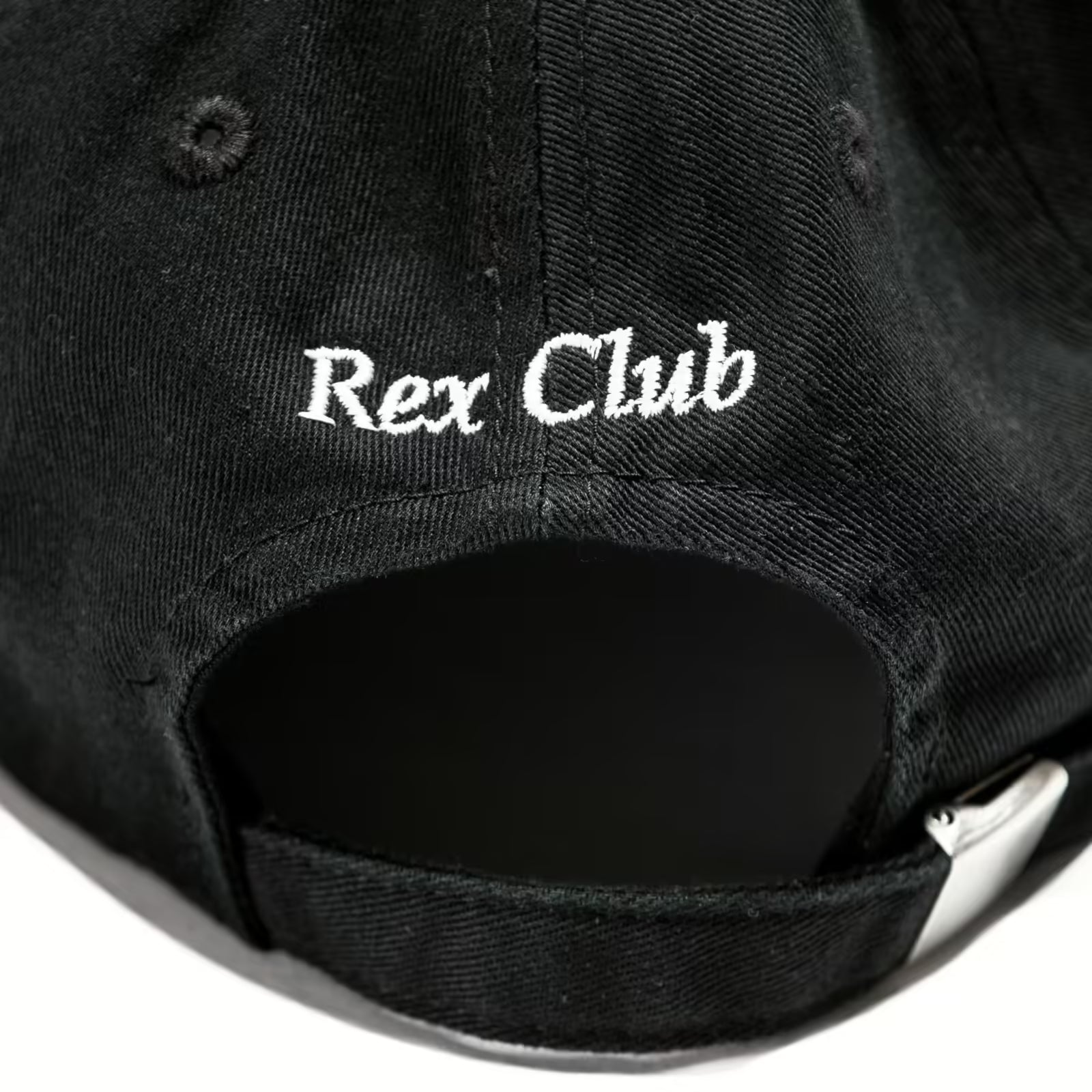 Rex Club | A close-up of the OFFSEASON 23 Slouch by Rex Club, a black 100% cotton slouch fit hat with "Rex Club" white embroidery on the back and an adjustable strap featuring a silver buckle. | Custom Caps | Custom Hats | Team Headwear | UK