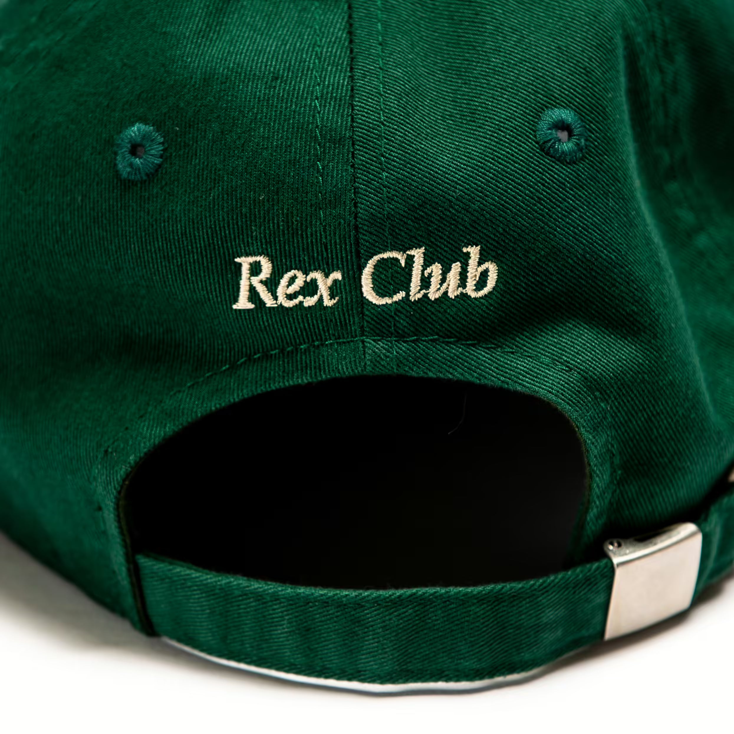 Rex Club | A close-up of the back of a green Rex Club OFFSEASON 23 Slouch cap, made from 100% cotton, with "Rex Club" embroidered in beige above the adjustable strap and metal buckle, highlighting its classic slouch fit. | Custom Caps | Custom Hats | Team Headwear | UK