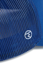 Rex Club | Close-up of blue mesh fabric from the RC 26 Trucker by Rex Club, showcasing a small white circular embroidered logo with a stylized lightning bolt at the center. | Custom Caps | Custom Hats | Team Headwear | UK