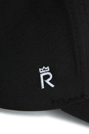 Rex Club | Close-up of RC 26 Performance black jersey by Rex Club, highlighting a white embroidered “R” monogram crowned with a small symbol—signature detail on sports apparel. | Custom Caps | Custom Hats | Team Headwear | UK