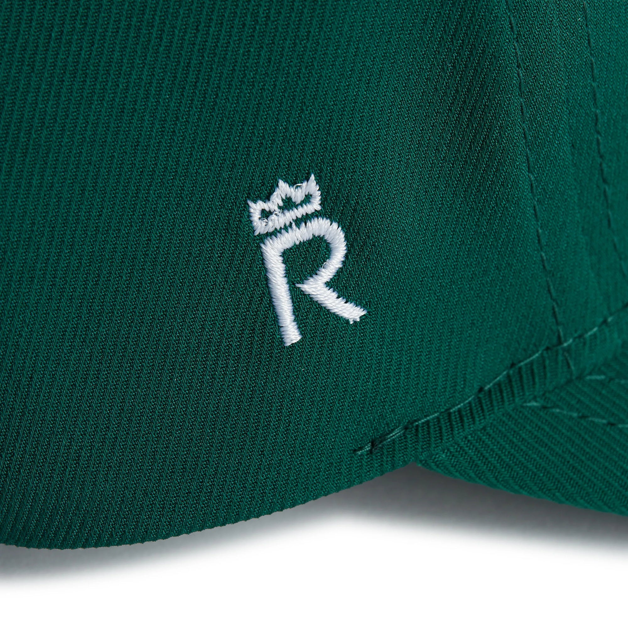 Rex Club | Close-up of the green RC 26 Performance jersey fabric by Rex Club, featuring a white embroidered "R" topped with a crown—a stylish, sporty monogram detail. | Custom Caps | Custom Hats | Team Headwear | UK