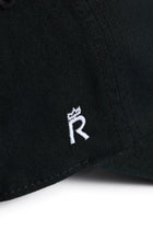 Rex Club | A close-up of the Rex Club Labor Et Ludus cap, crafted from 100% black cotton fabric and featuring a small white embroidered crowned “R” emblem. One size fits most. | Custom Caps | Custom Hats | Team Headwear | UK