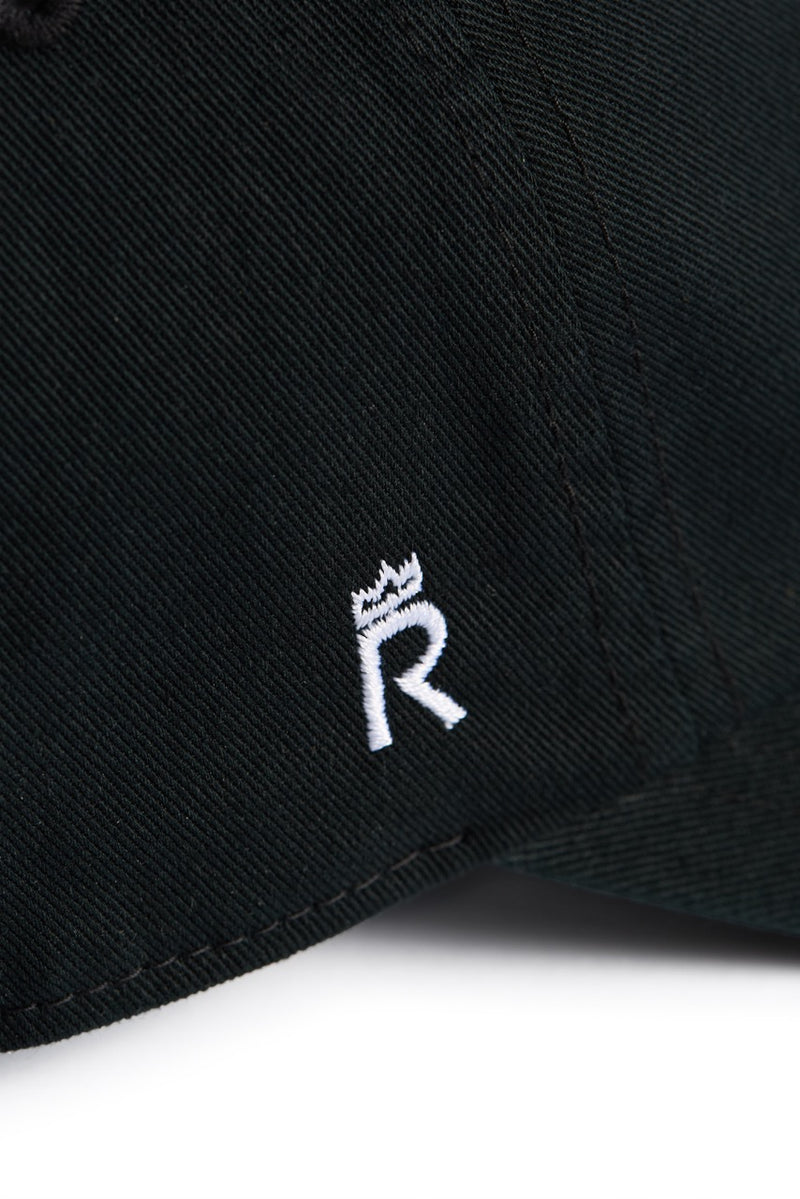 Rex Club | A close-up of the Rex Club Labor Et Ludus cap, crafted from 100% black cotton fabric and featuring a small white embroidered crowned “R” emblem. One size fits most. | Custom Caps | Custom Hats | Team Headwear | UK