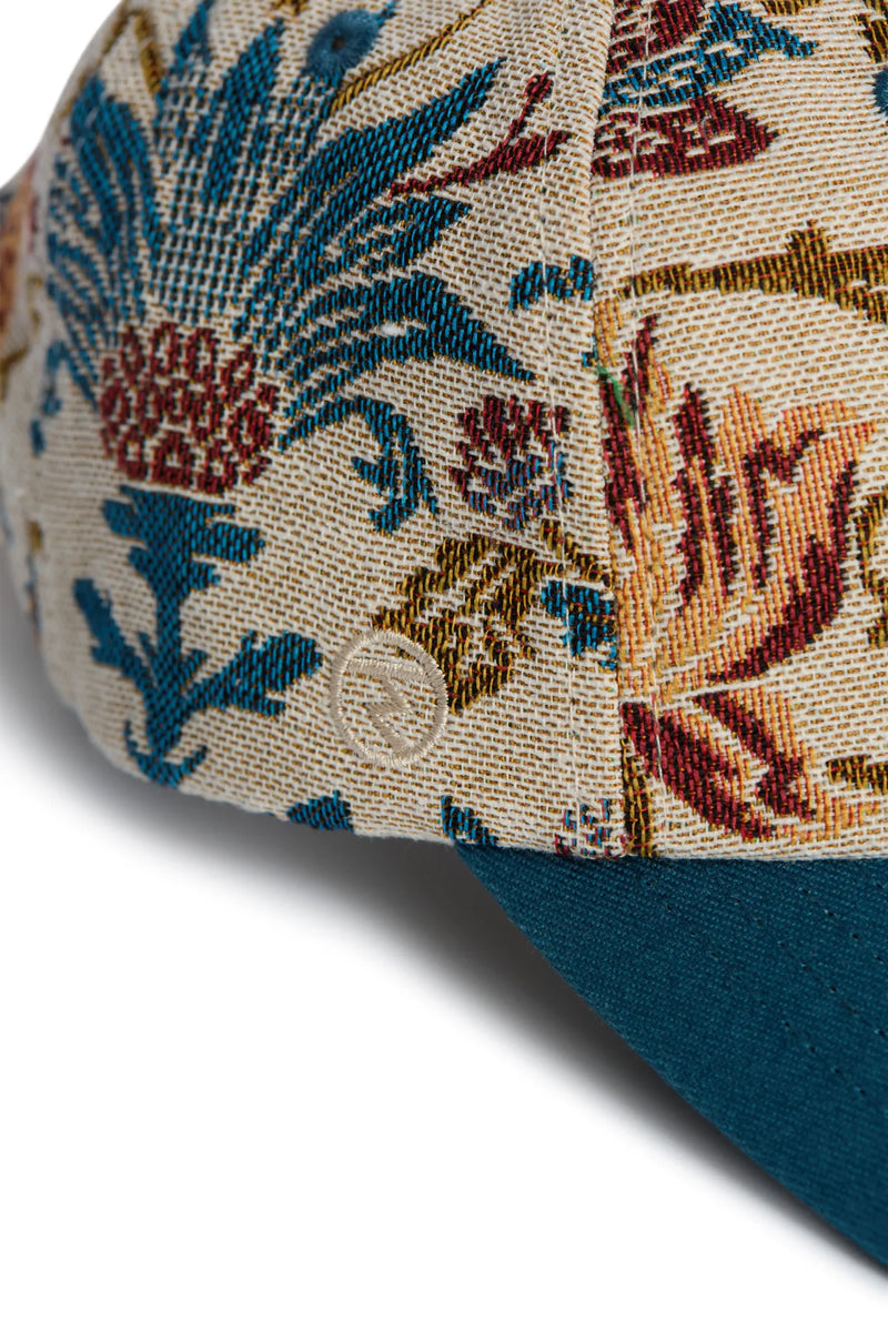 Rex Club | Close-up of the Rex Club "A New Day" cap, featuring a blue, red, and gold floral tapestry on beige with a solid teal bill. The woven fabric’s texture showcases the premium quality of this bespoke accessory. | Custom Caps | Custom Hats | Team Headwear | UK variant-1
