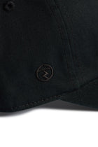 Rex Club | Close-up of the Rex Club MTRC - Black cap, showcasing its subtle stitching and a small circular embroidered logo with a horizontal line and upward arrow near the curved brim—part of the exclusive Manchester Tennis & Racquets Club merchandise collection. | Custom Caps | Custom Hats | Team Headwear | UK