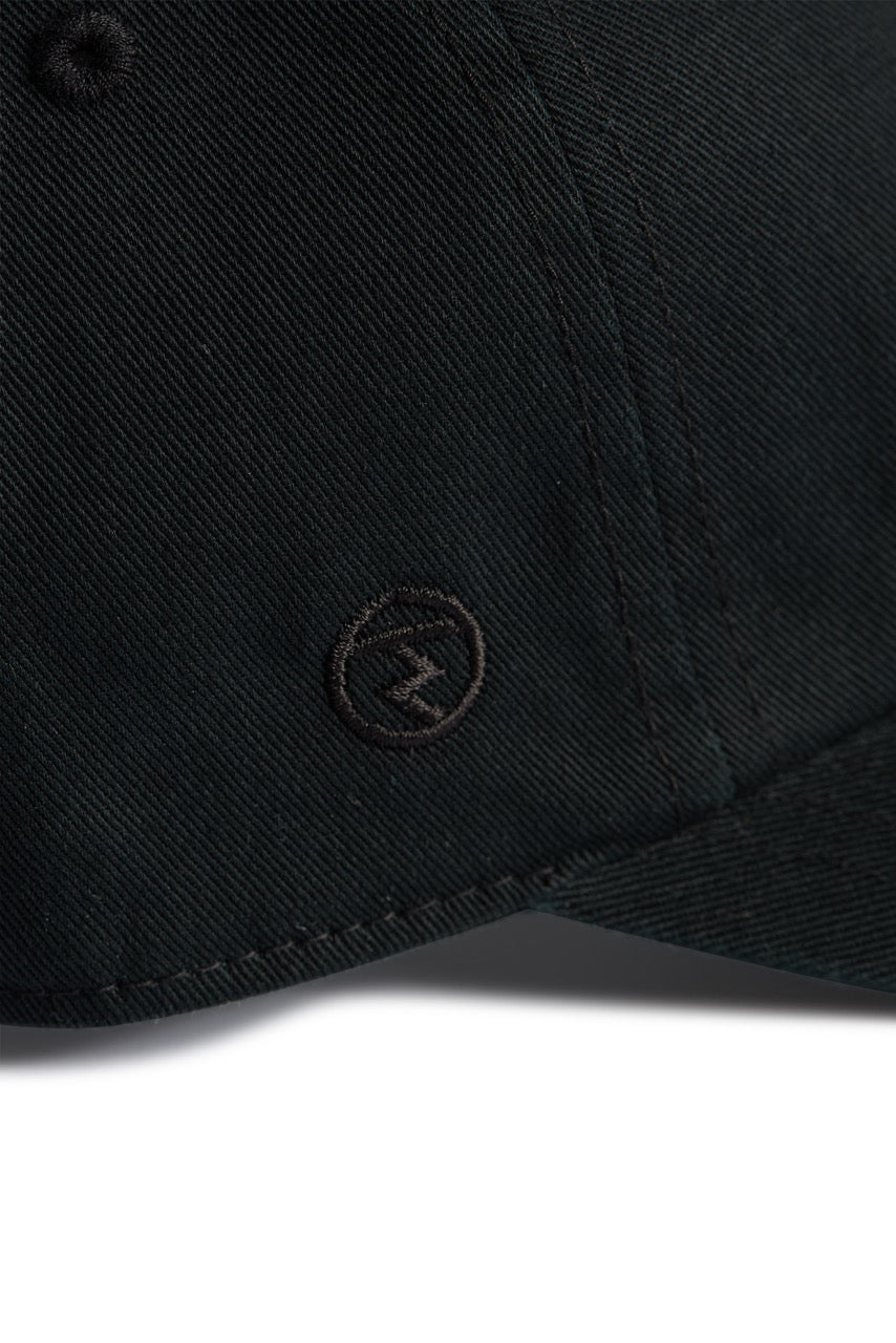 Rex Club | Close-up of the Rex Club MTRC - Black cap, showcasing its subtle stitching and a small circular embroidered logo with a horizontal line and upward arrow near the curved brim—part of the exclusive Manchester Tennis & Racquets Club merchandise collection. | Custom Caps | Custom Hats | Team Headwear | UK