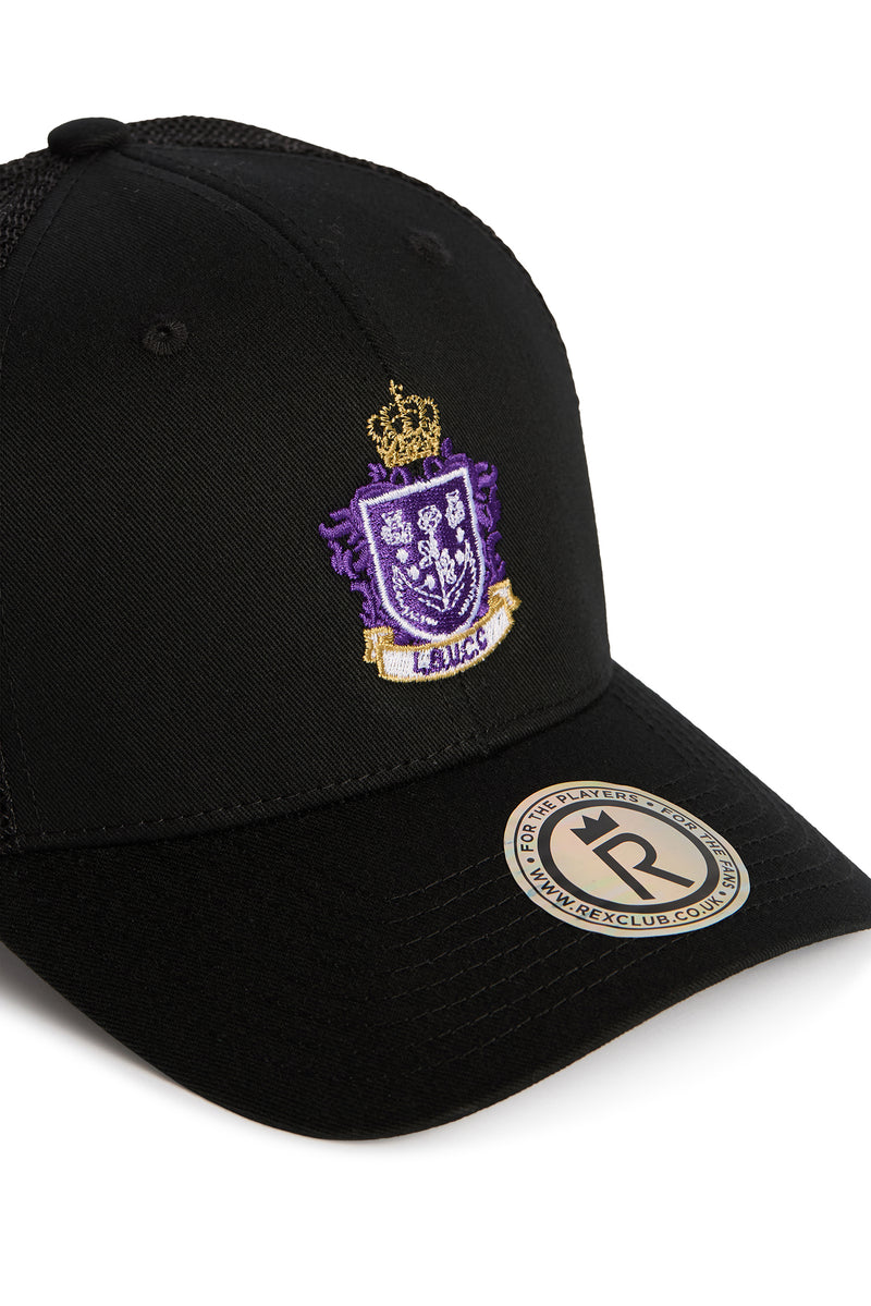 Rex Club | Here is a rewritten version of the sentence using your product data: The Leeds Beckett University Cricket Club Trucker by Rex Club is a black baseball cap made from a durable polyester-cotton blend, adorned with a purple and gold embroidered crest featuring a crown. A round sticker on the brim displays text encircling a bold “R”. | Custom Caps | Custom Hats | Team Headwear | UK