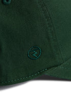 Rex Club | Close-up of the MTRC - Green club cap by Rex Club, crafted from dark green cotton and featuring a small embroidered circle logo with a lightning bolt near the brim—a refined detail that distinguishes this cap. | Custom Caps | Custom Hats | Team Headwear | UK