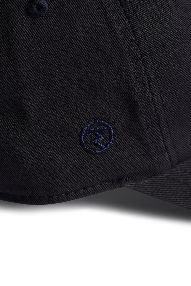 Rex Club | Close-up of a navy blue MTRC - Navy cap by Rex Club, featuring a small embroidered circular logo on the side of the brim—ideal for fans seeking official Manchester Tennis & Racquets Club merchandise for their collection. | Custom Caps | Custom Hats | Team Headwear | UK