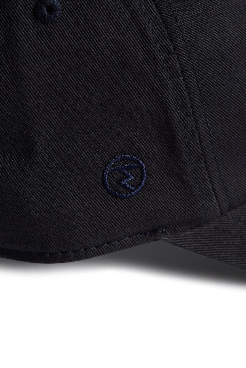 Rex Club | Close-up of a navy blue MTRC - Navy cap by Rex Club, featuring a small embroidered circular logo on the side of the brim—ideal for fans seeking official Manchester Tennis & Racquets Club merchandise for their collection. | Custom Caps | Custom Hats | Team Headwear | UK