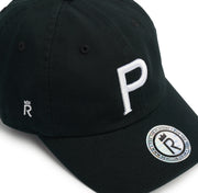 Rex Club | The Cornish Pirates - P Slouch by Rex Club is a black cap with a bold white "P" on the front, a small crowned "R" on the side, and a silver "REXCLUB.COM" sticker—bringing Champ Rugby spirit and Cornish Pirates flair to your style. | Custom Caps | Custom Hats | Team Headwear | UK
