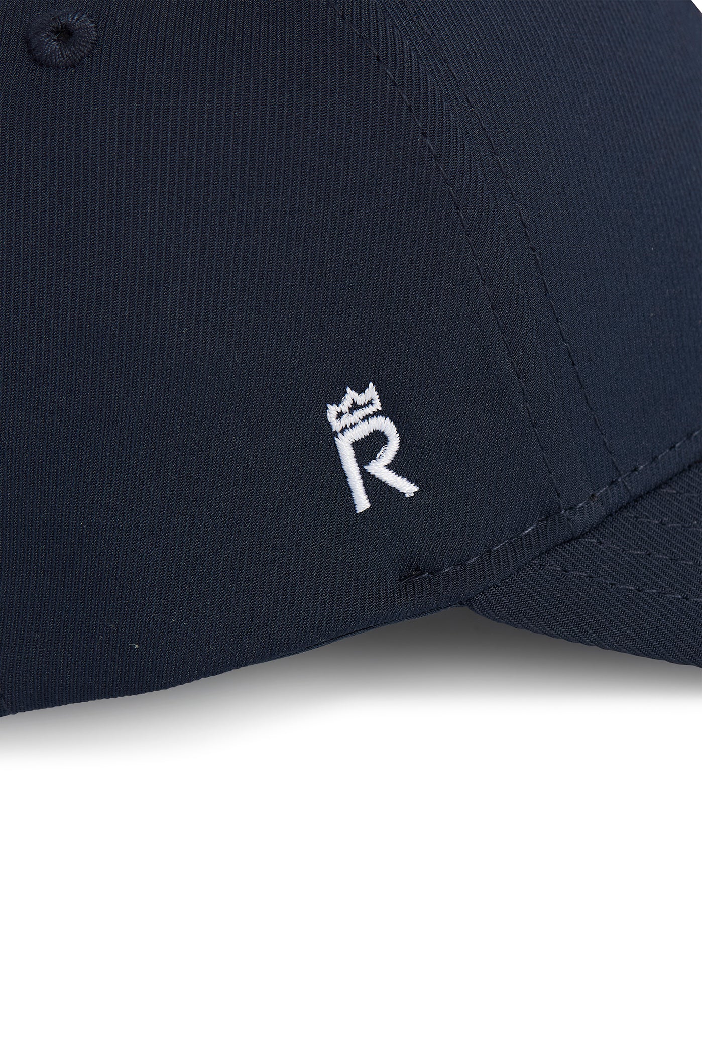 Rex Club | Close-up of the Rex Club Clydach CC Stretch cap in navy blue, showcasing a small white embroidered “R” with a crown above it on the front panel. Crafted from a premium polyester-cotton-spandex blend, this fitted cap delivers a comfortable stretch fit for all-day wear. | Custom Caps | Custom Hats | Team Headwear | UK