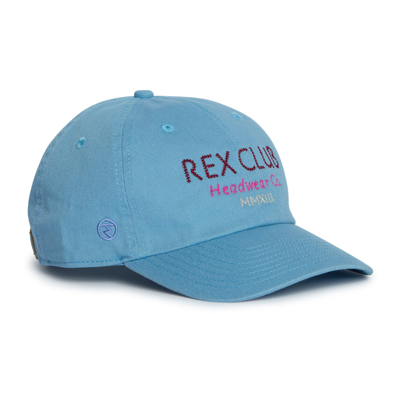 Rex Club | Introducing the “In the details - Cornflower” cap by Rex Club—a light blue, 100% cotton slouch cap featuring “REX CLUB Headwear Co. MANILA” embroidered in vibrant purple and red on the front. A small purple circular logo accents the left side near the brim, making this summer-ready hat an ideal choice for those who value both comfort and style. | Custom Caps | Custom Hats | Team Headwear | UK