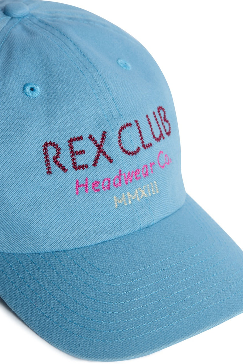 Rex Club | Introducing In the details - Cornflower by Rex Club: a light blue cotton slouch cap designed for summer, featuring “REX CLUB” embroidered in bold red, “Headwear Co.” in soft pink, and “MMXIII” in vibrant yellow across the front. | Custom Caps | Custom Hats | Team Headwear | UK