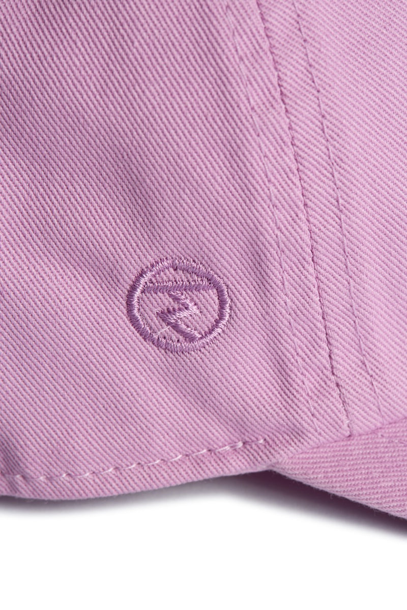 Rex Club | Close-up of the Rex Club “In the details - Parma Violet” cap, showcasing pink fabric with visible stitching and an embroidered circular logo featuring a stylized “R” in the center. | Custom Caps | Custom Hats | Team Headwear | UK