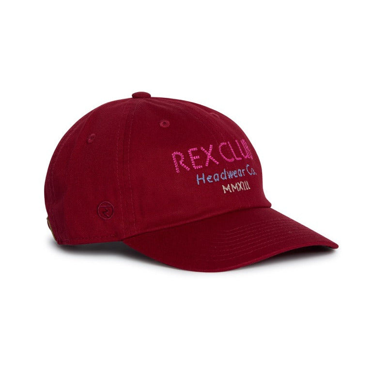 Rex Club | Introducing the “In the details - Tyrian” cap by Rex Club—a maroon slouch baseball cap crafted from 100% cotton, featuring a curved brim and visible seams on the crown. The front showcases “REX CLUB Headwear Co. MMXXIII” embroidered in vibrant pink and purple, making this comfortable hat a standout piece for your summer collection. | Custom Caps | Custom Hats | Team Headwear | UK