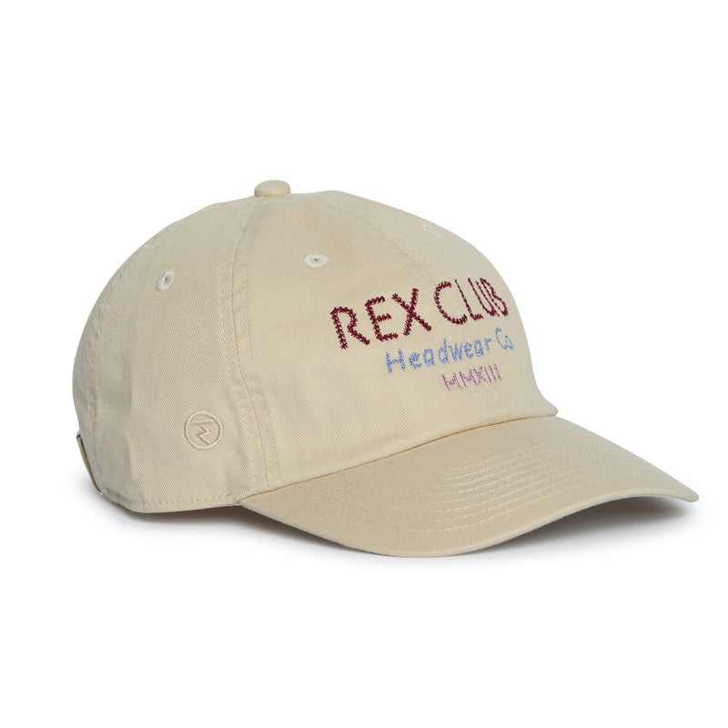 Rex Club | Introducing the “In the details - Cotton” cap by Rex Club—a beige baseball cap crafted from soft cotton. Featuring “REX CLUB Headwear Co. MMXIII” embroidered in red, purple, and yellow on the front, this cap showcases a curved brim and visible stitching details, making it an essential addition to your summer accessories collection. | Custom Caps | Custom Hats | Team Headwear | UK