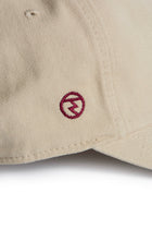 Rex Club | A close-up of the Rex Club RC 3d 26 - Beige cotton slouch cap, showcasing a small, circular red 3D embroidered logo with a stylized lightning bolt inside. | Custom Caps | Custom Hats | Team Headwear | UK